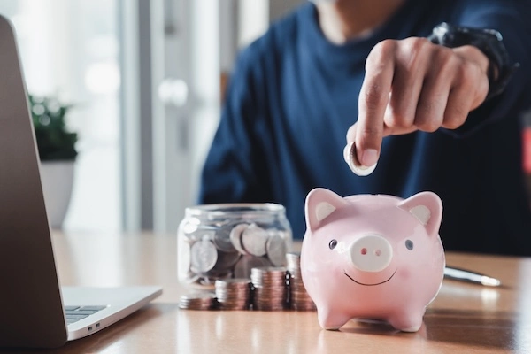 Person saving money in a piggy bank, symbolizing the initial savings from choosing budget roofers with potential hidden long-term costs.