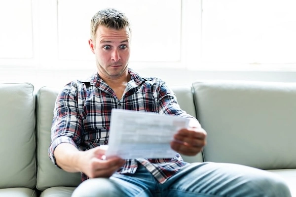 Man in a plaid shirt looking shocked while reading a document, symbolizing the unexpected high costs of premium roofing options.