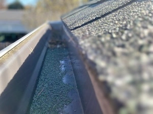 Close-up image showing granules accumulated in a gutter from deteriorating shingles, highlighting the need for roof inspection and potential replacement.